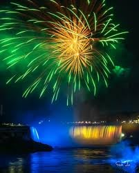 Fireworks exploding over Niagara Falls at night with illuminated cascading water in blue and gold lighting