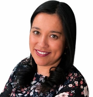 Professional headshot of a woman with dark hair and pink lipstick wearing a dark floral patterned top against a white background