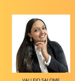 Professional portrait of Vallejo Salome, a woman with long black hair wearing a black blazer and white shirt, smiling with her hand near her face against a yellow background